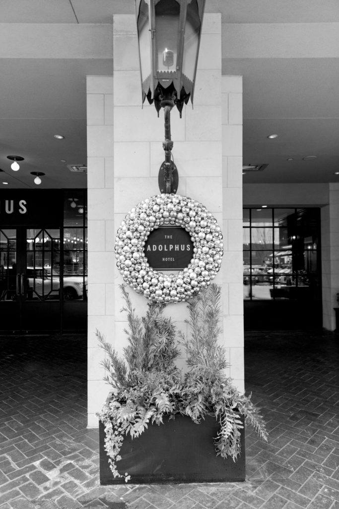 Elegant nameplate on the entryway of The Adolphus Hotel with a golden wreath surrounding it along with a lamp on top and plants at the bottom