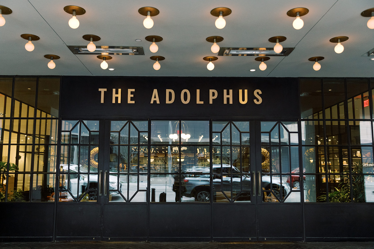 The grand lobby of the hotel with the view of the Dallas streets along with a sign on top of the doors that reads The Adolphus