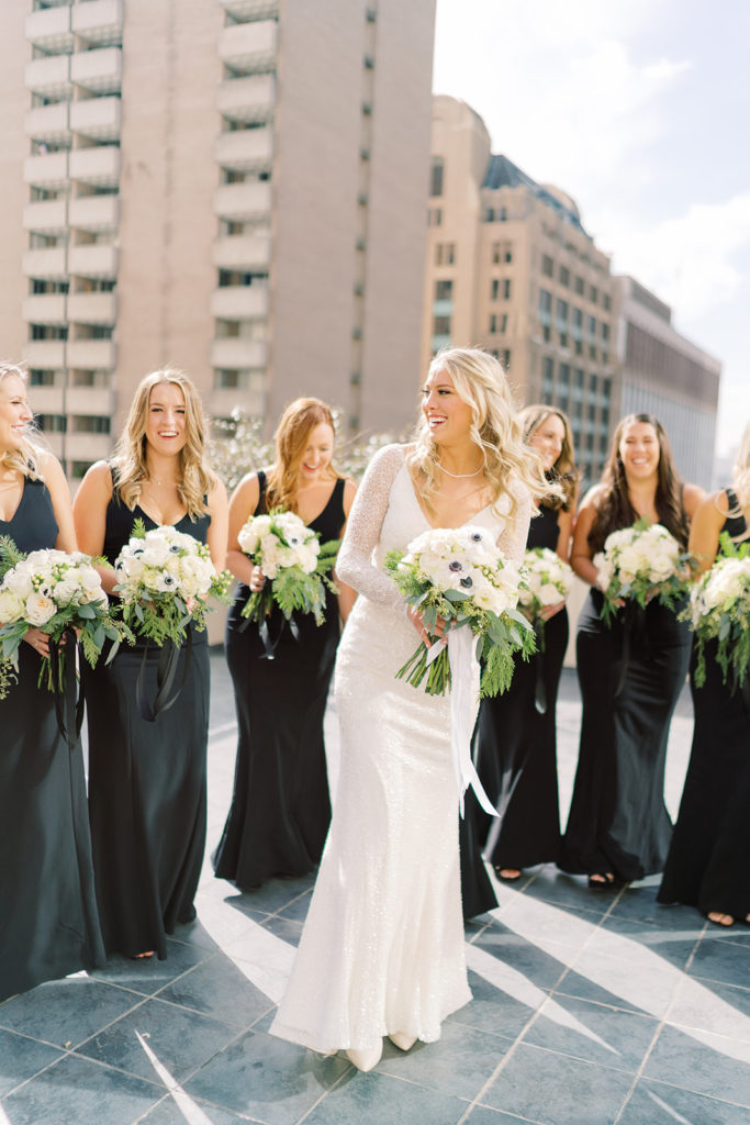 Bride smiles as she is surrounded by her bridesmaids as they all hold their floral bouquets, photographed by Texas wedding photographer Mackenzie Reiter