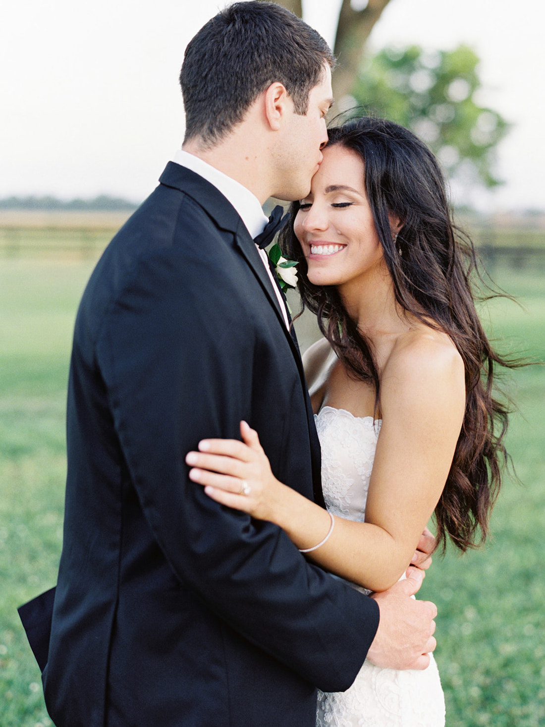 Groom kisses bride on the forehead as she smiles during their wedding held at the Dallas Arboretum, taken by Mackenzie Reiter