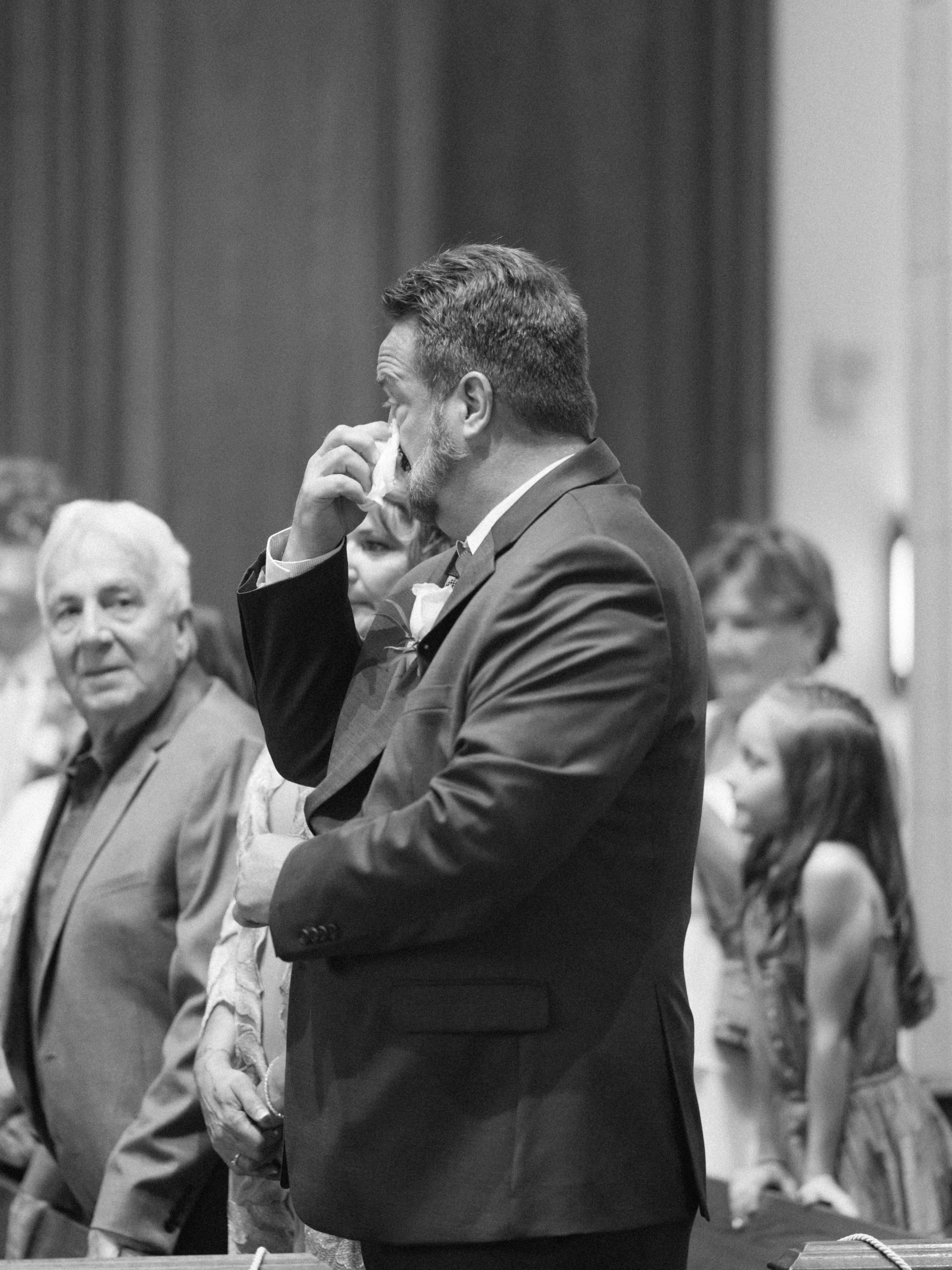 father of the groom wipes tears from eye during catholic wedding ceremony