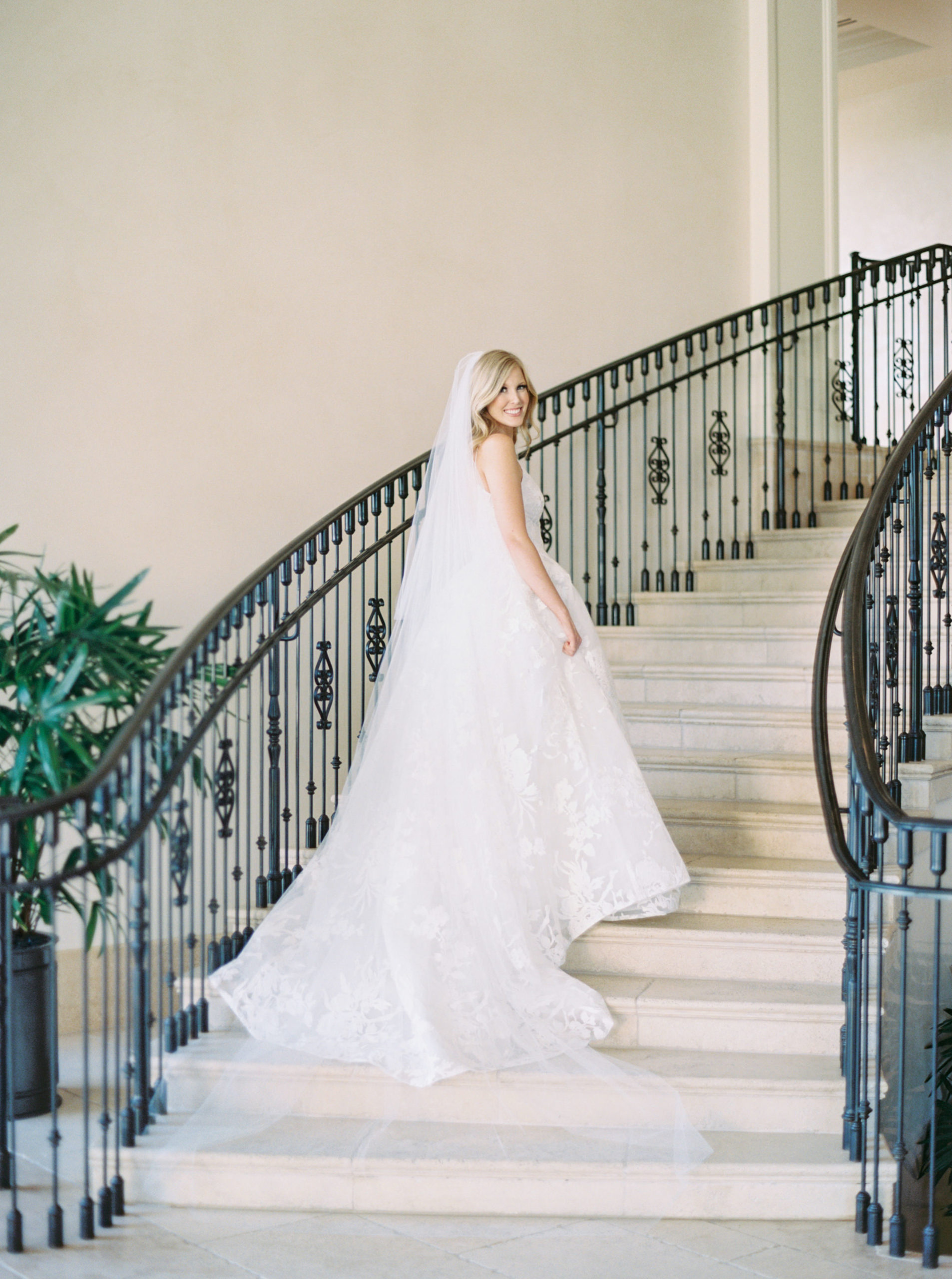 The stunning bride walking up the sweeping double staircase with iron-wrought railing at the Lakeside Country Club taken by Mackenzie Reiter Photography