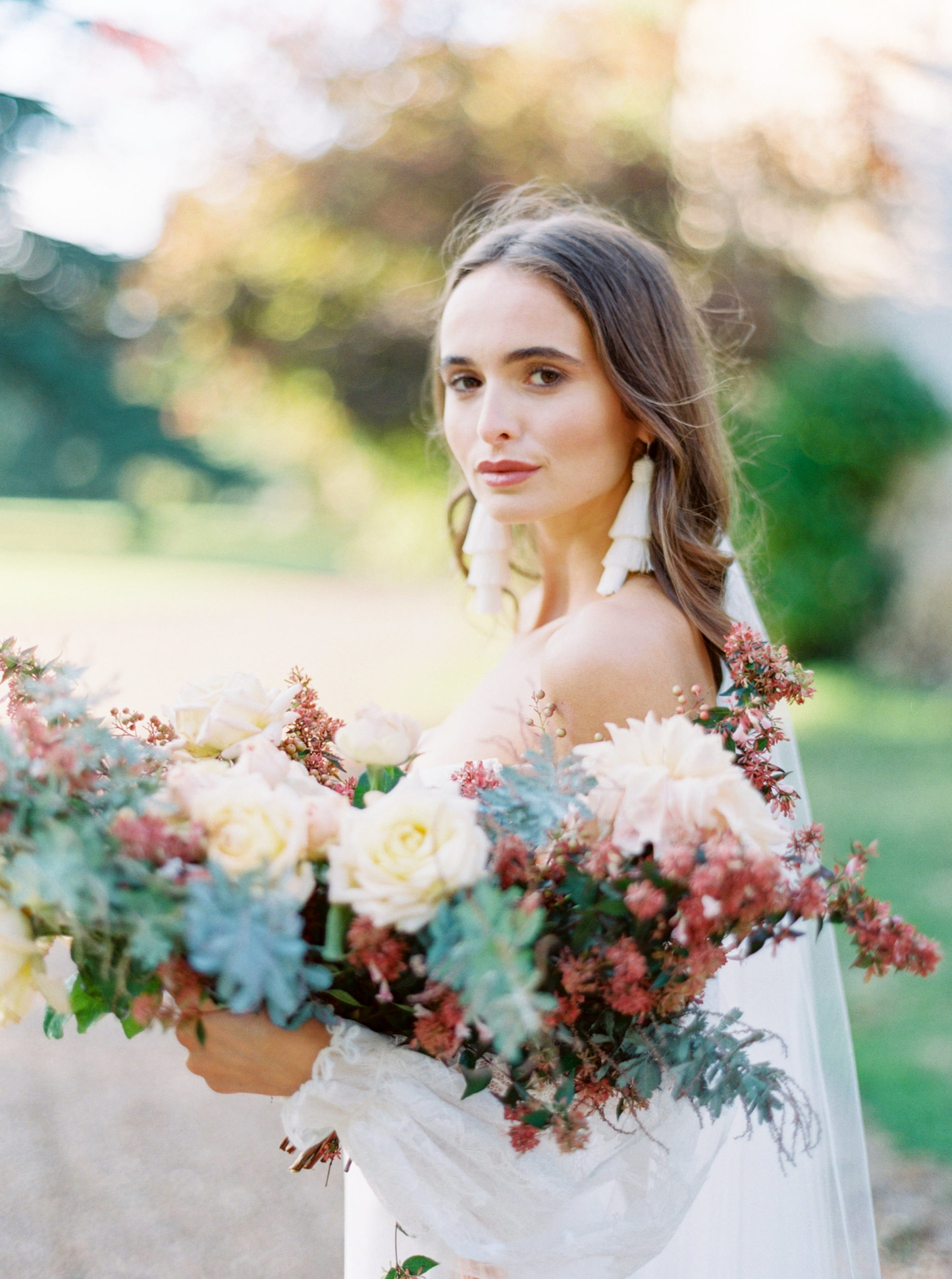 Bride gazing at the camera enchantingly while holding her stunning bouquet of flowers, taken by Mackenzie Reiter
