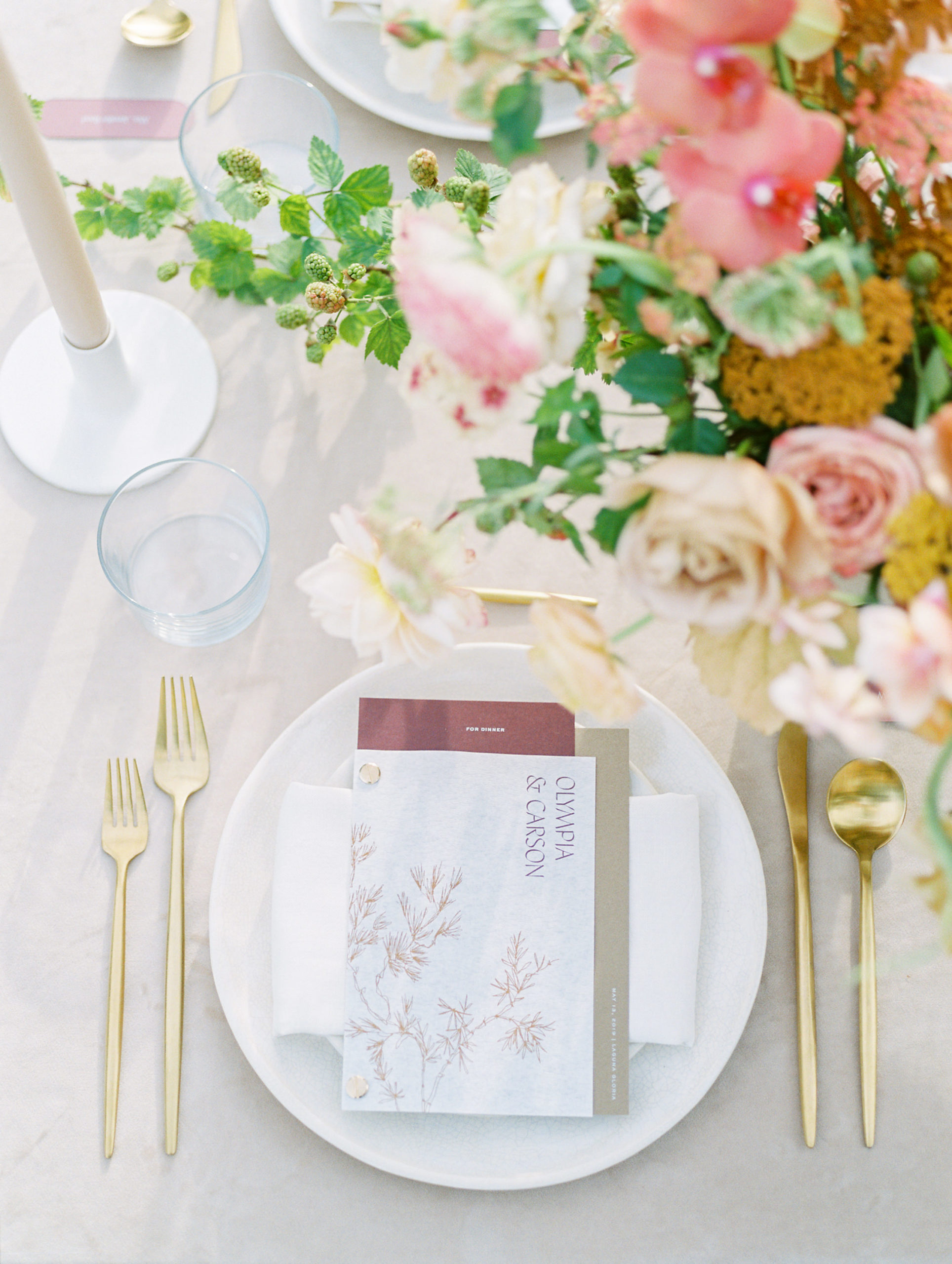 Close-up shot of the wedding reception table with a floral centerpiece, a plate, napkin and a menu with golden utensils