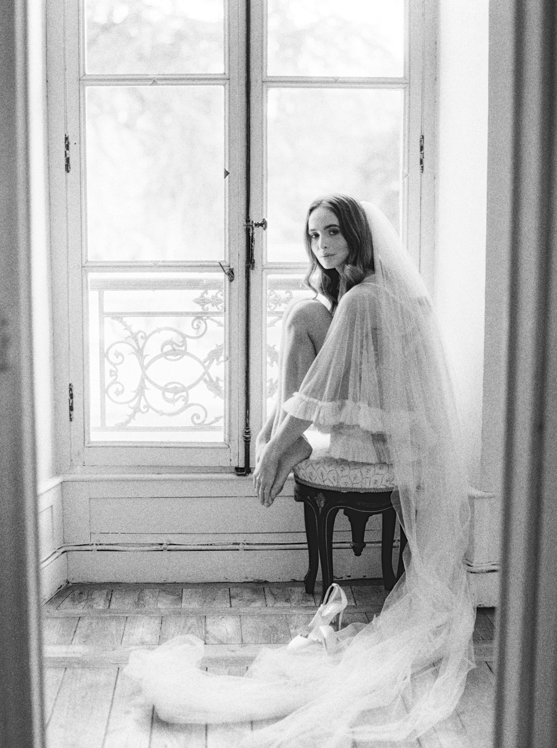Black and white photo of the bride sitting on a chair with her veil on
